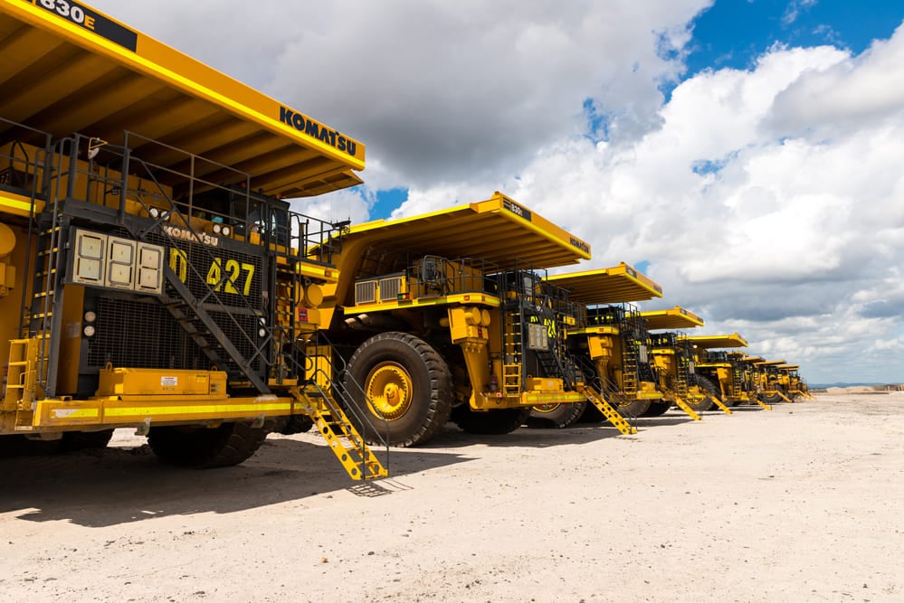A row of large yellow Komatsu dump trucks parked in a line on a mining site.